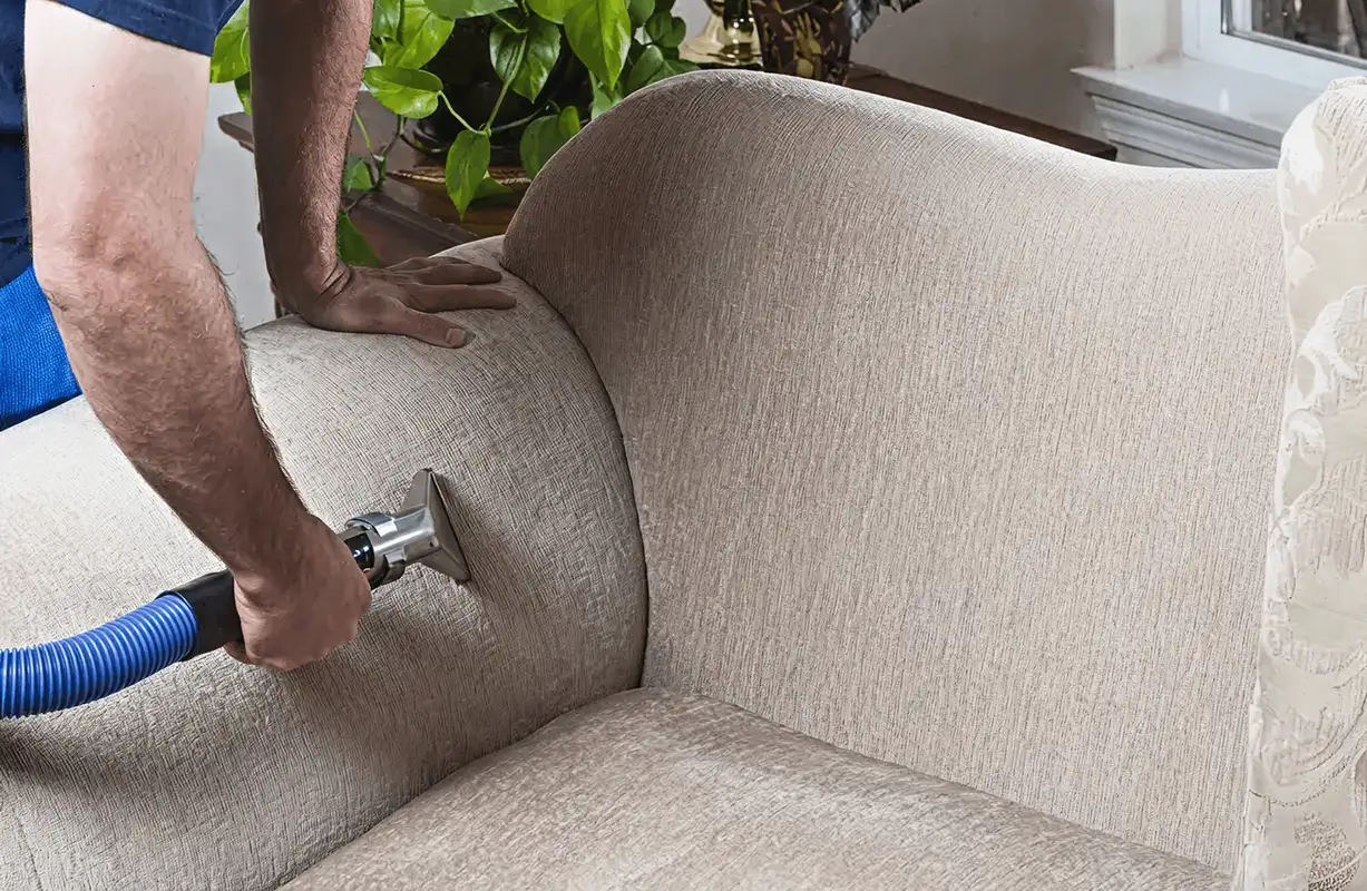 Professional upholstery cleaner deep-cleaning a fabric sofa with a handheld extraction tool and hose, Milwaukee, WI.